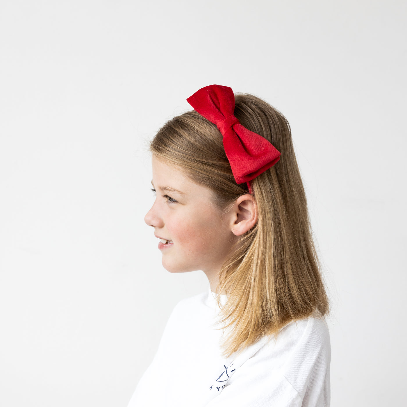 Smiling little girl wearing classic style red, velvet Alice band with bow