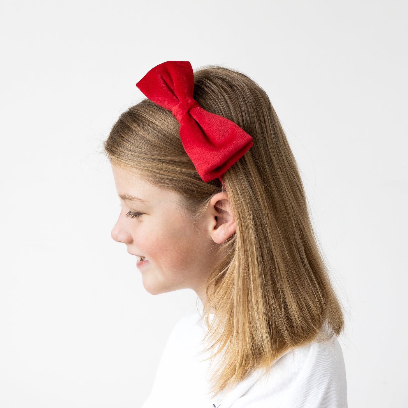 Close up image of a red velvet bow Alice band worn by a dark blonde little girl