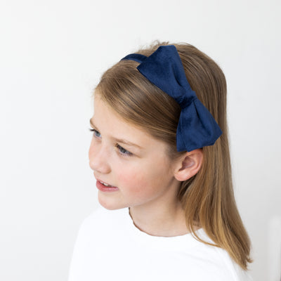 Little girl wearing large navy bow Alice band in velvet fabric