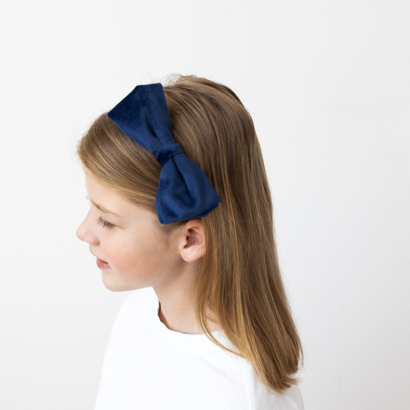 Side profile of dark blonde little girl wearing a navy velvet Alice band with side bow