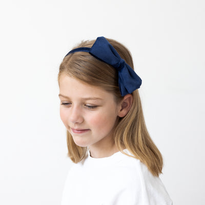 Smiling girl looking down showing the velvet navy  Alice band she is wearing featuring a large side bow