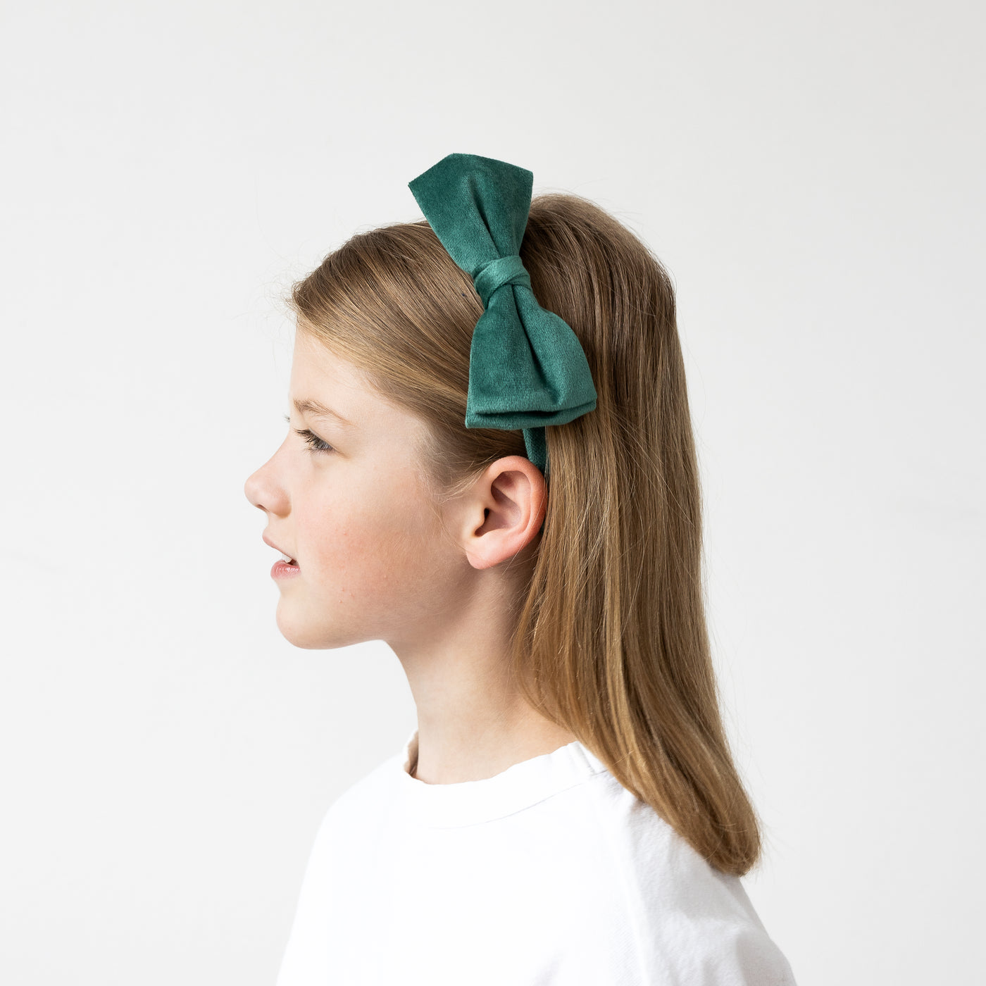 Side profile of dark blonde girl wearing green velvet bow Alice band