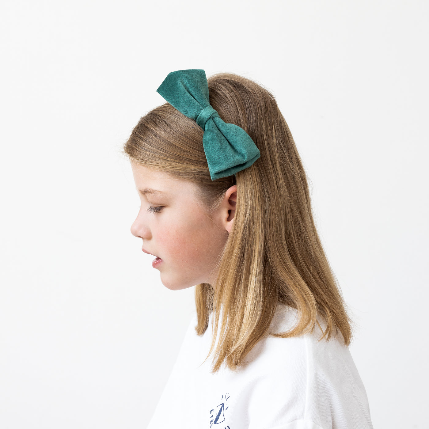 Little girl looking downwards wearing a velvet green bow Alice band