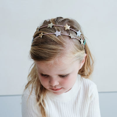 Thoughtful image of a little blonde girl wearing a pretty double ribbon wrapped Alice band with glitter padded stars
