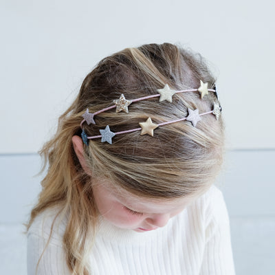 Close up photo of a little girl wearing a metallic and glitter star playful Alice band