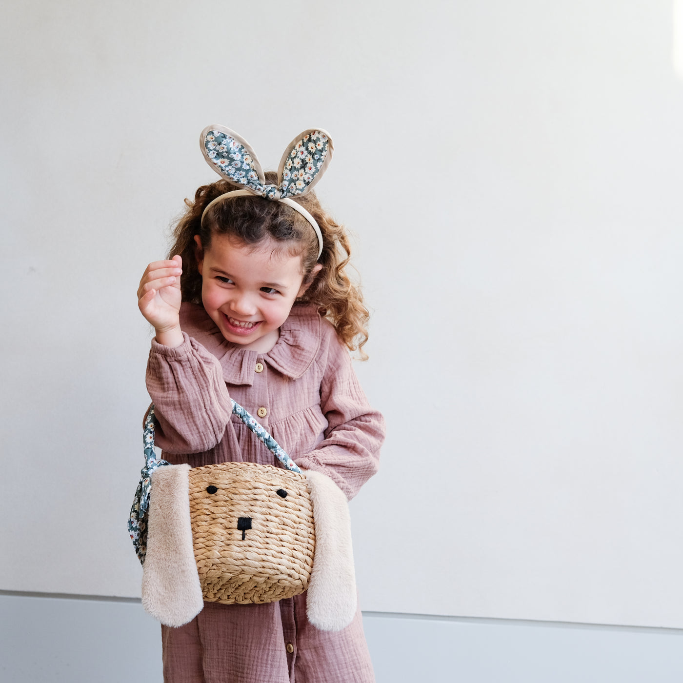 Little girl with a cheeky smile wearing bunny ears headband with pretty Easter basket