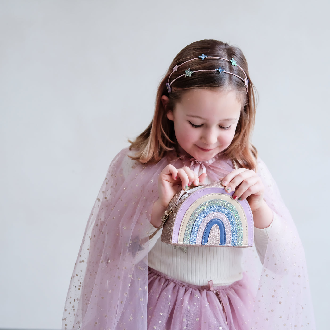 Little girl wearing a double Alice band with glitter rainbows and stars peering into a colourful rainbow bag
