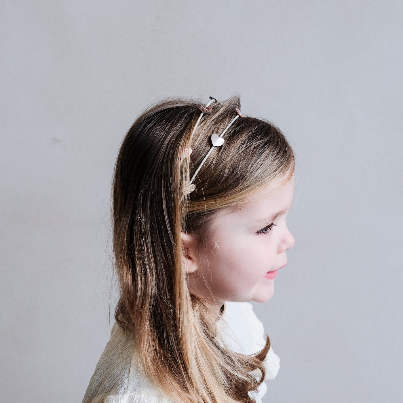 Side profile of a little girl wearing a sweet Alice band with hearts