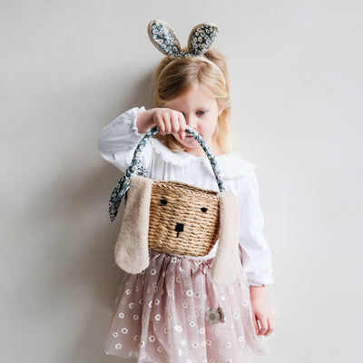 Little girl looking at an Easter basket, wearing daisy print floral bunny rabbit ears headband