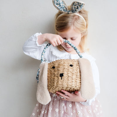 Little blonde girl wearing sweet floral bunny ears headband looking into Easter bunny basket
