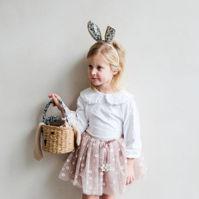 Little blonde girl wearing Easter bunny fabric ears holding an Easter basket, wearing a daisy print tutu