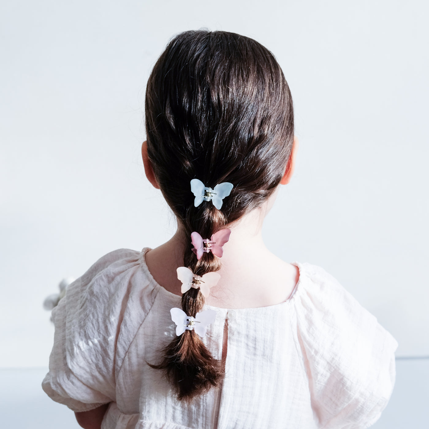 Dark haired little girl with hair worn in a pony tail secured by pretty butterfly shape bulldog clips