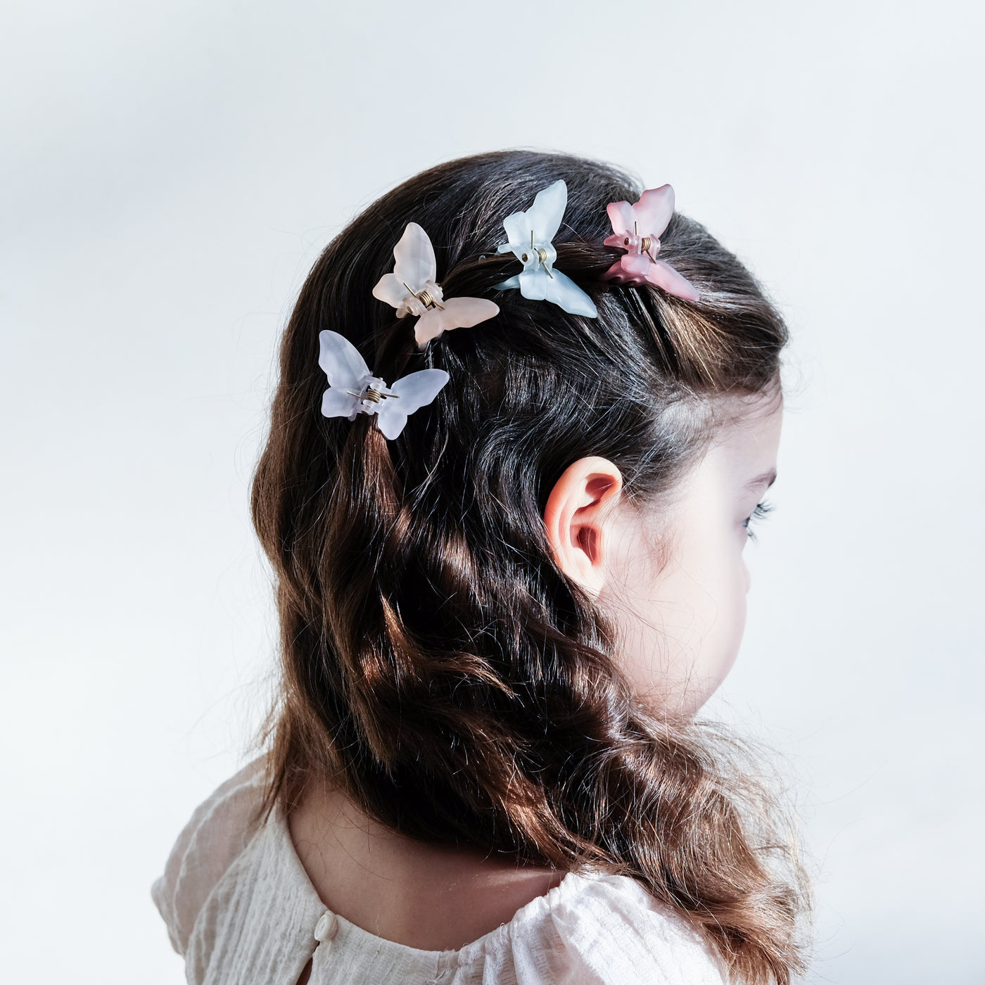 Dark haired little girl wearing pastel coloured butterfly shape bulldog clips to one side