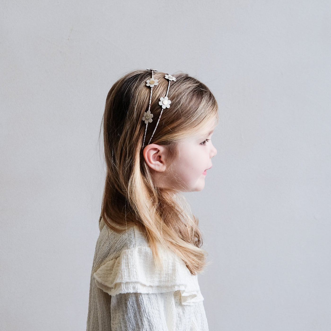Side profile of little girl wearing a double Alice band with daisies 