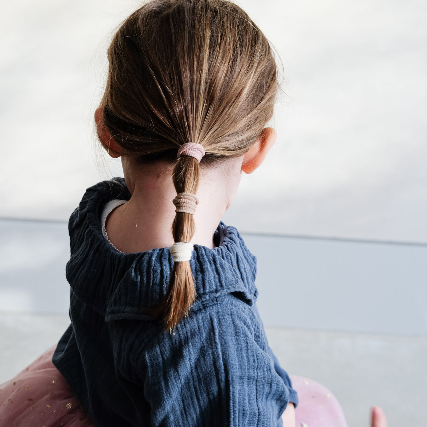 Little girl wearing soft and stretchy, neutral toned, towelling ponies in a low ponytail 