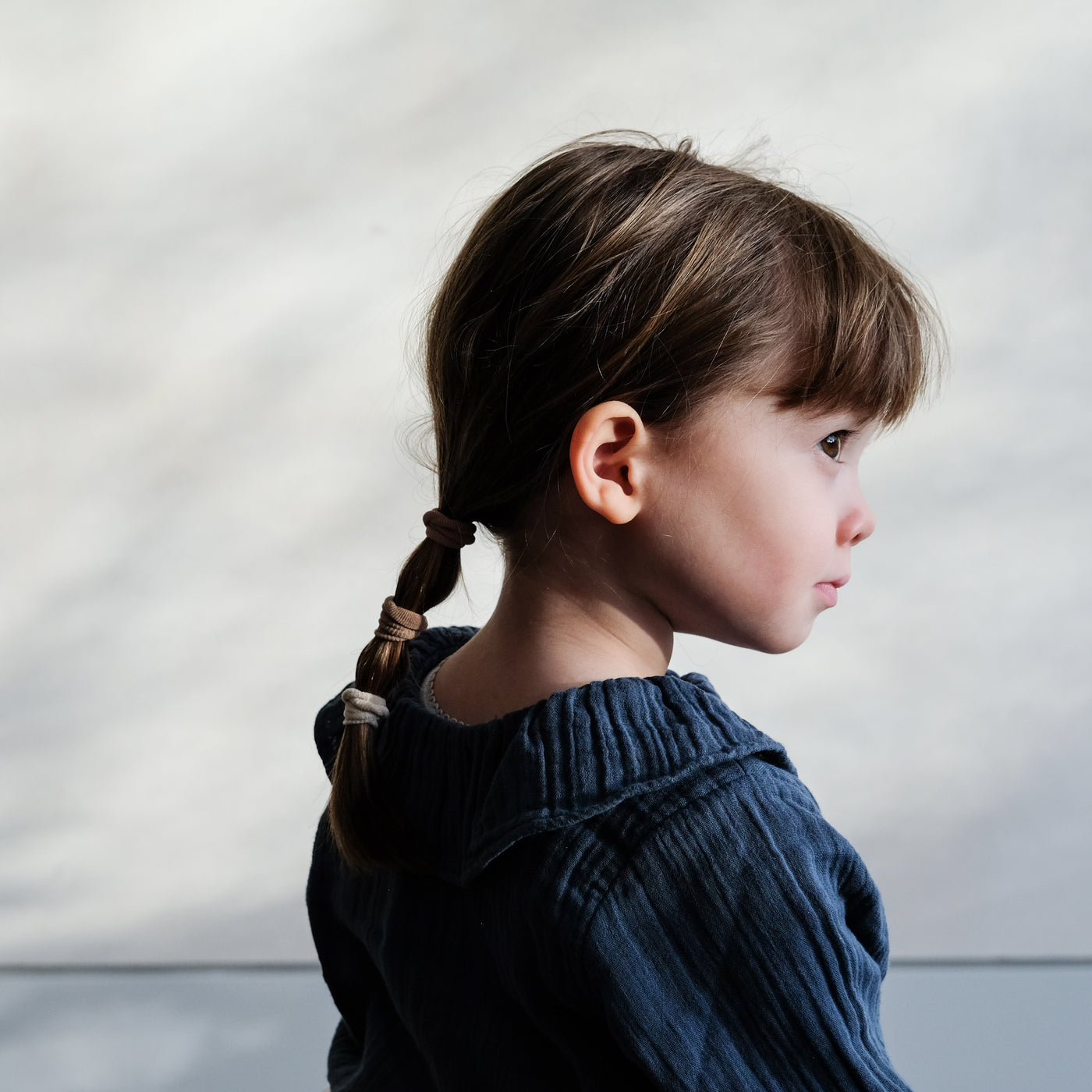 Side profile of little girl with cute fringe wearing soft mini towelling ponies styled in a low ponytail