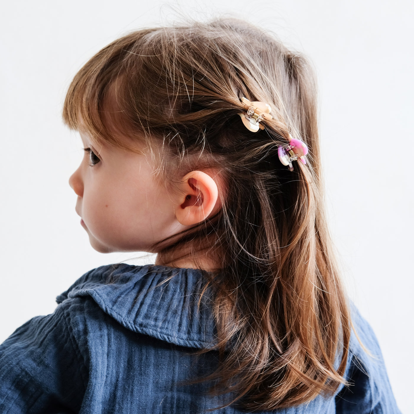 Sweet little dark haired girl looking over her shoulder showing hair clipped back by two colourful, fun little heart shaped bulldog clips