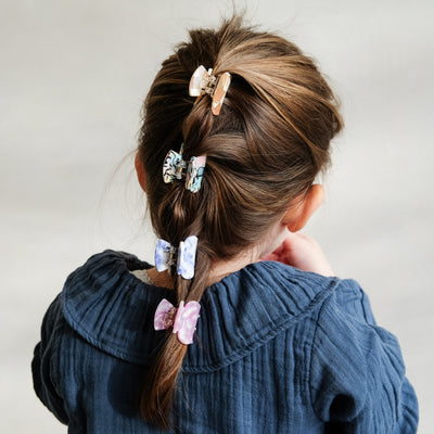 Dark haired little girl with French plait effect hair style held together with four bright and colourful mini bulldog clips