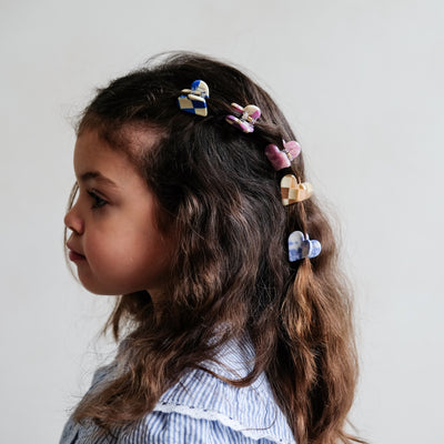 Side profile of a little girl with thick, dark curly hair clipped back with four heart shaped bulldog clips in bright and fun colours and patterns