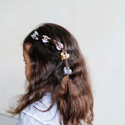 Dark haired little girl with one section of hair clipped back using a selection of five mini heart shaped, colourful bulldog clips