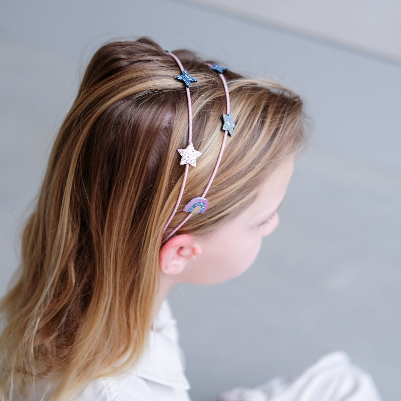 Blonde little girl wearing an Alice band featuring glitter stars and rainbows