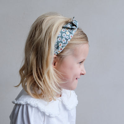Side profile of little blonde girl wearing floral bow Alice band