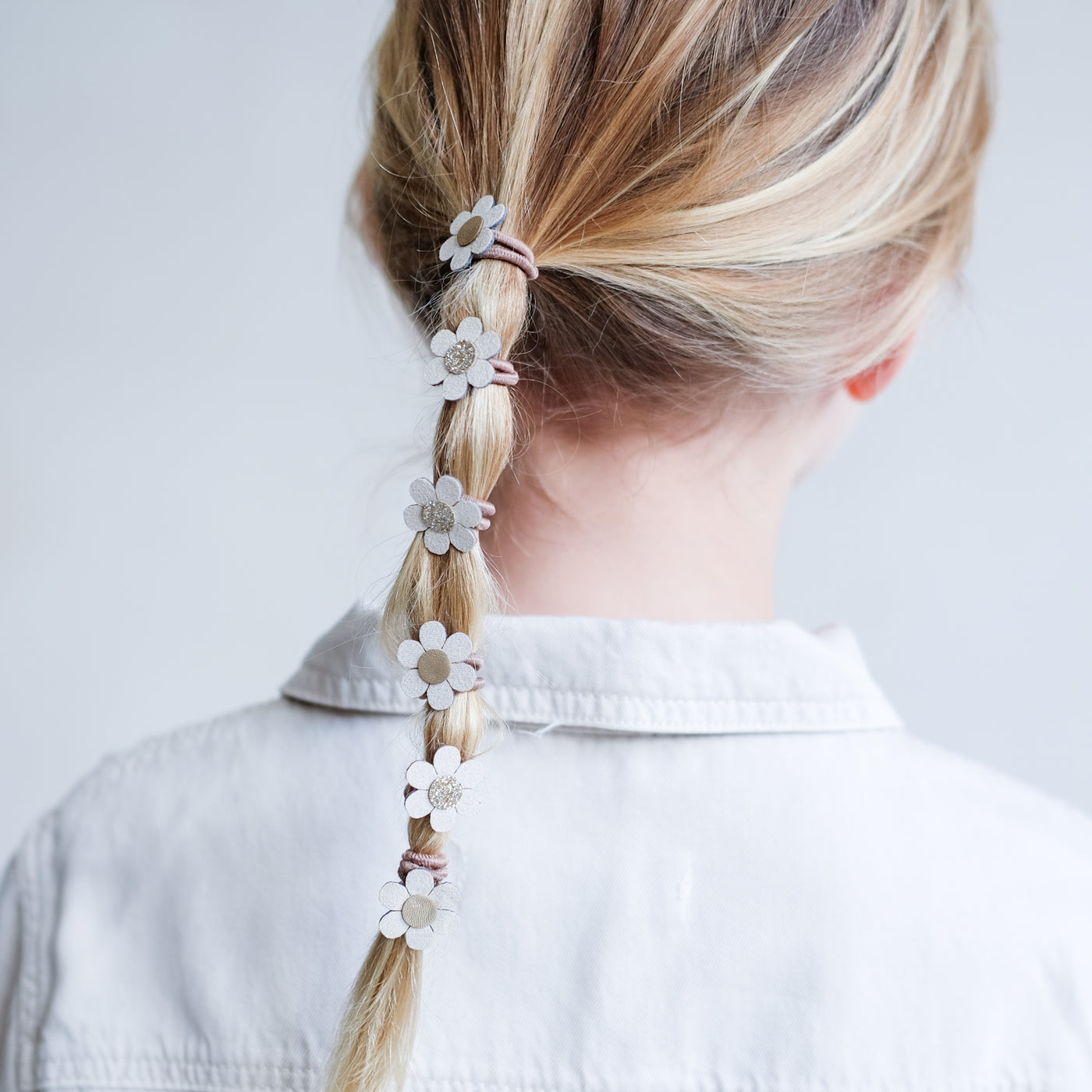 Mini cream daisy ponies worn in a ponytail hairstyle by little girl with fine blonde hair
