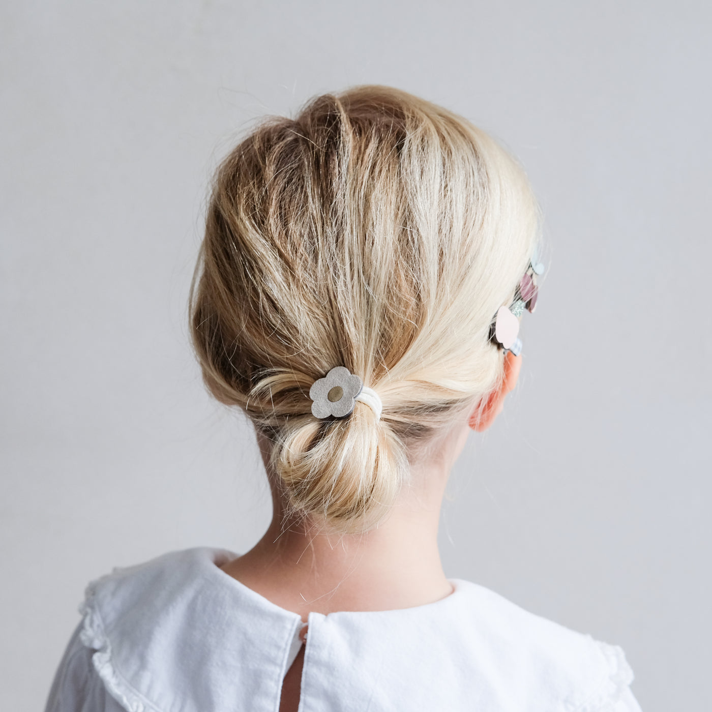 Soft suedette flower pony with metallic gold centre, worn by little girl in a cute low bun hairstyle