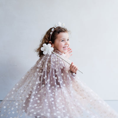 Little girl twirling in a daisy print cape holding a daisy wand and wearing a daisy flower headdress