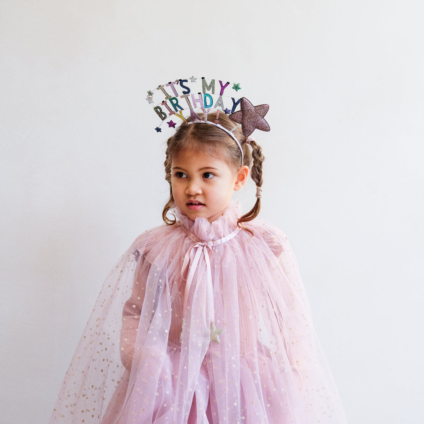 Little girl wearing birthday celebration headdress and pink cape