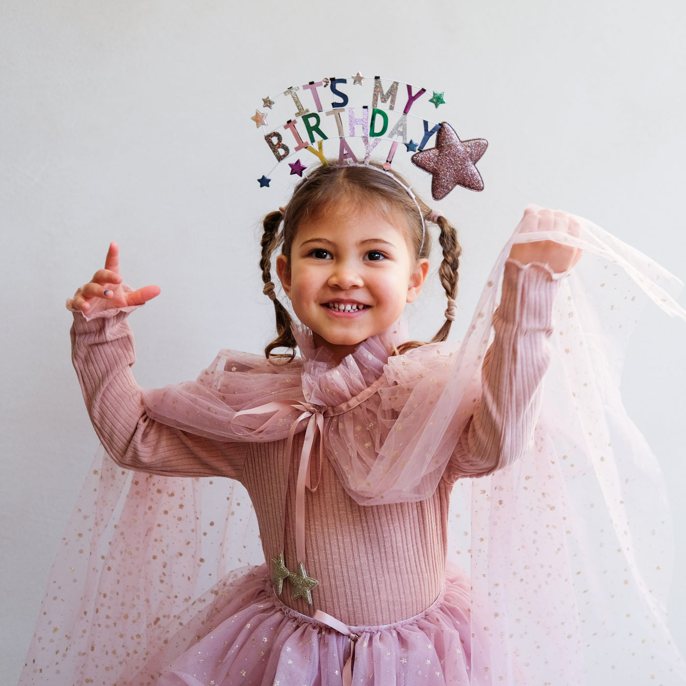 Little girl dancing wearing a pretty birthday celebration headdress in multicolour