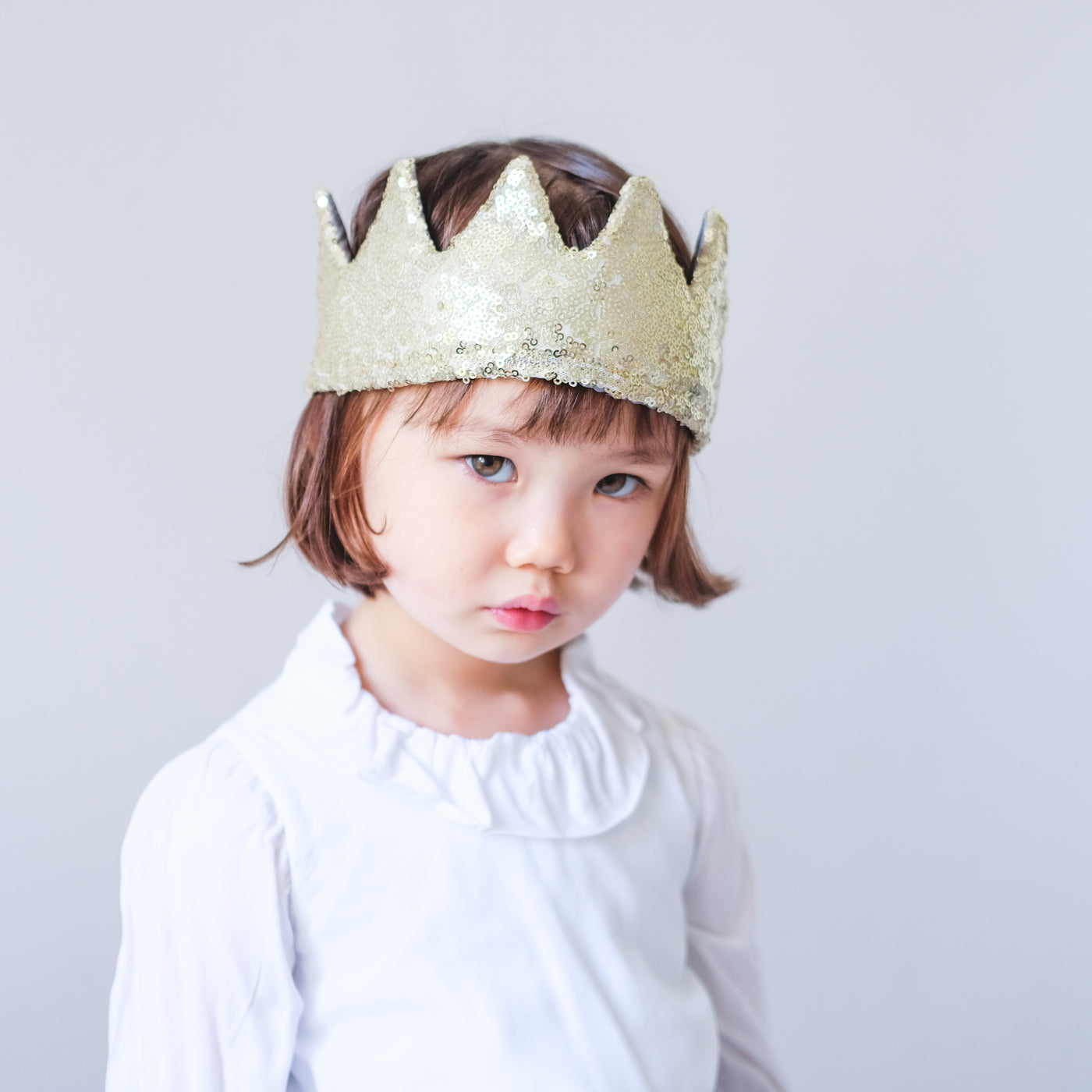 Little dark haired girl with bob haircut wearing a soft fabric sequin glitter crown