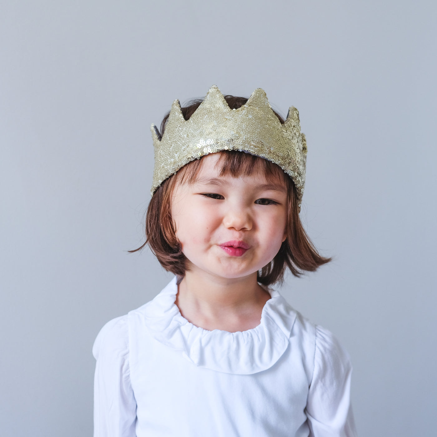 Little dark haired girl with a cheeky smile wearing a sequin gold fabric crown