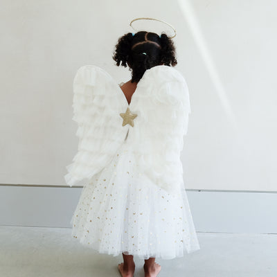 Dark haired little girl wearing a white tulle layered tutu, a gold halo headdress and a beautiful pair of angel wings