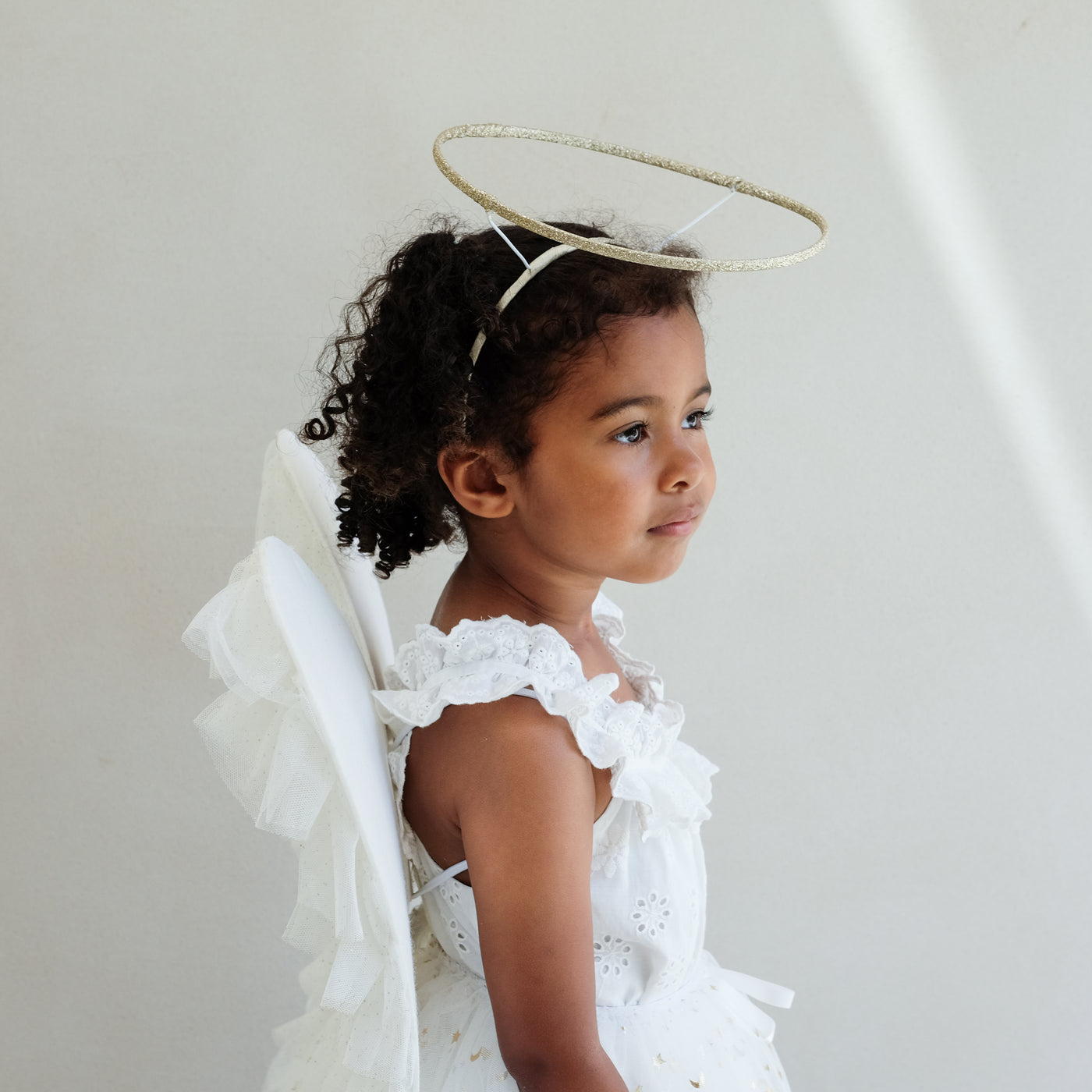 Dark haired little girl wearing a white tulle layered tutu, a gold halo headdress and a beautiful pair of angel wings