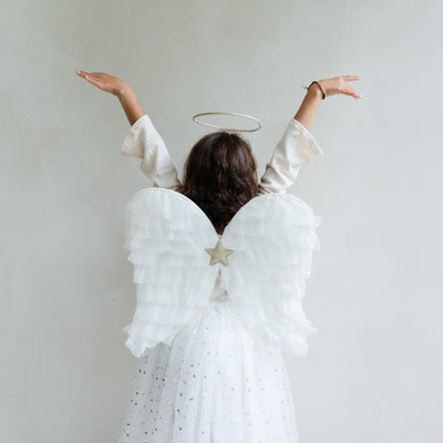 Dark haired little girl wearing a white tulle layered tutu, a gold halo headdress and a beautiful pair of angel wings