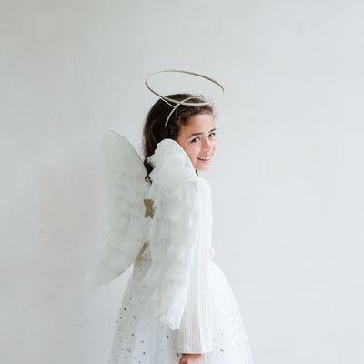 Dark haired little girl wearing a white tulle layered tutu, a gold halo headdress and a beautiful pair of angel wings