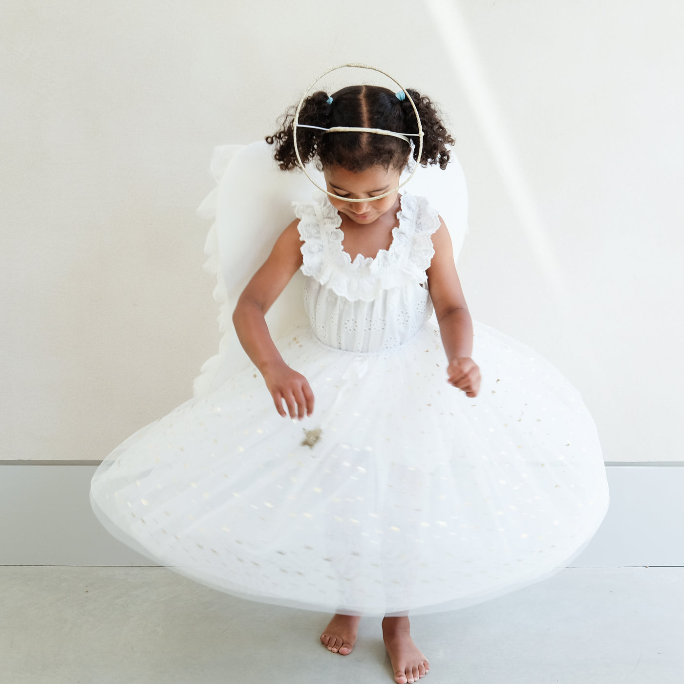 Dark haired little girl wearing a white tulle layered tutu, a gold halo headdress and a beautiful pair of angel wings