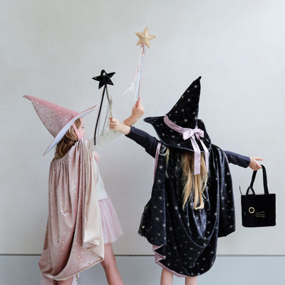 Two little girls dressed as witches, one in pink, one in black with star wands with ribbon trails and a black velvet cat trick or treat bag