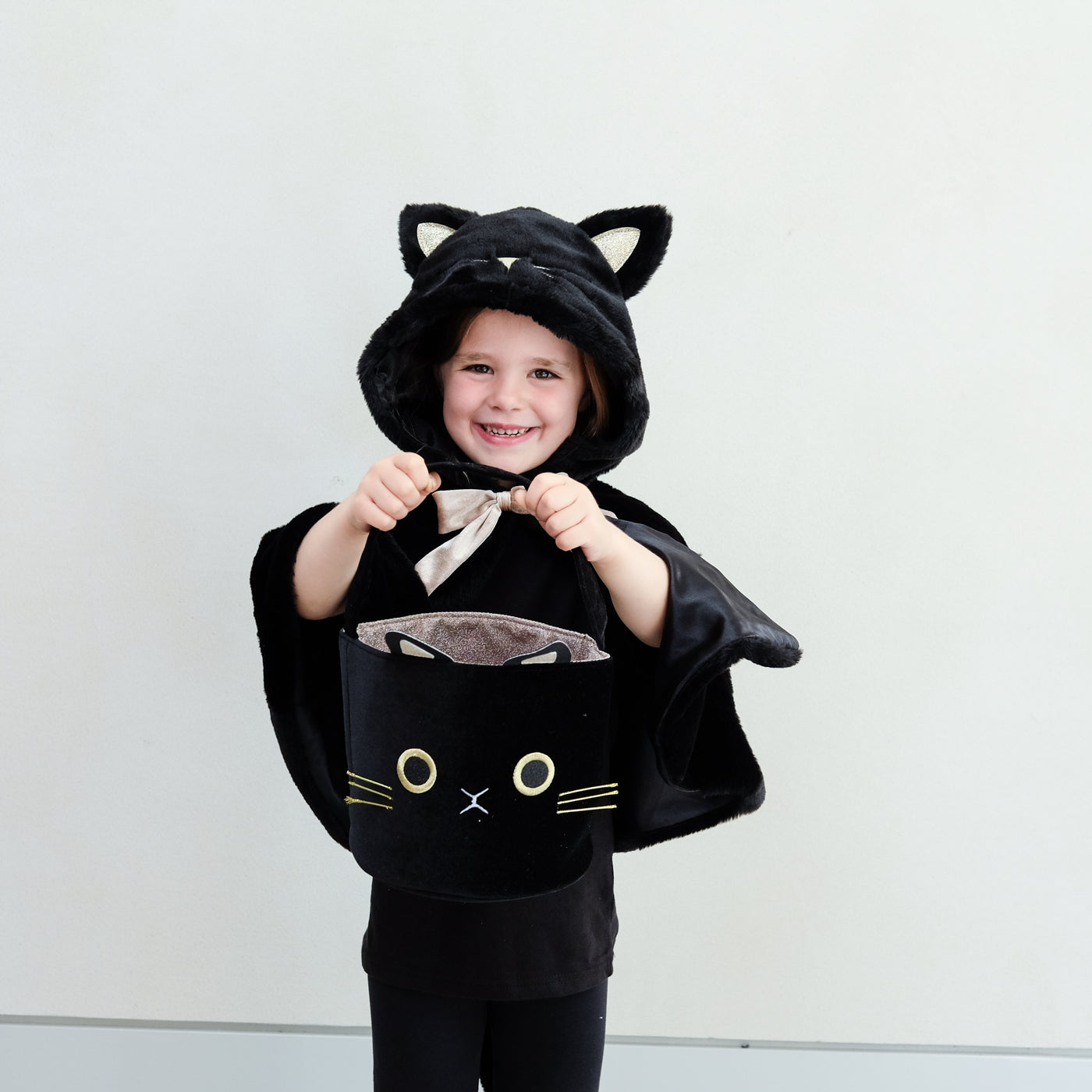 Little girl dressed up in a black fluffy cat cape with hood and satin bow tie holding a black cat face trick or treat bag