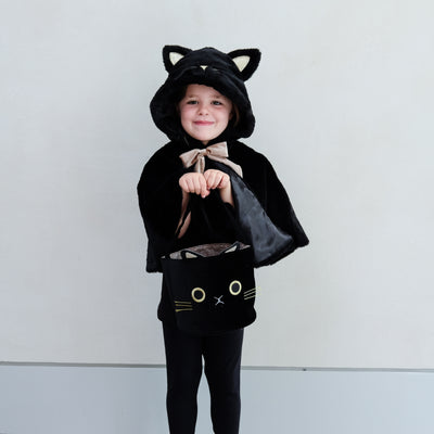 Little girl dressed up in a black fluffy cat cape with hood and satin bow tie holding a black cat face trick or treat bag