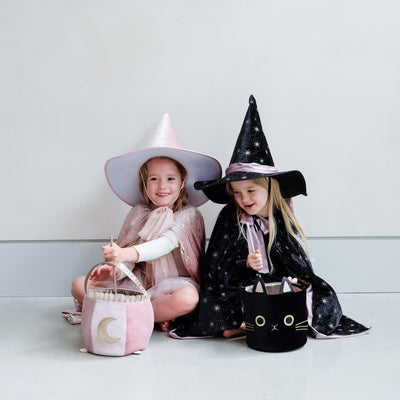 Two little girls dressed as witches, one in pink, one in black with star wands with ribbon trails and a black velvet cat trick or treat bag and pink velvet cauldron bag