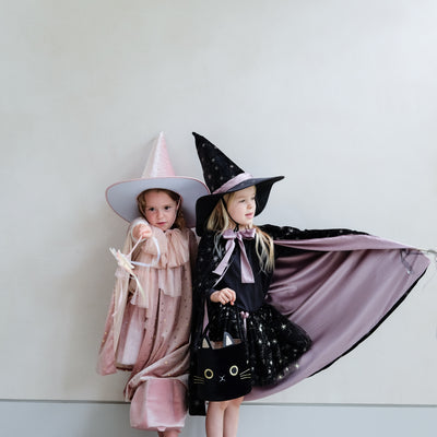 Two little girls dressed as witches, one in pink, one in black with star wands with ribbon trails and a black velvet cat trick or treat bag