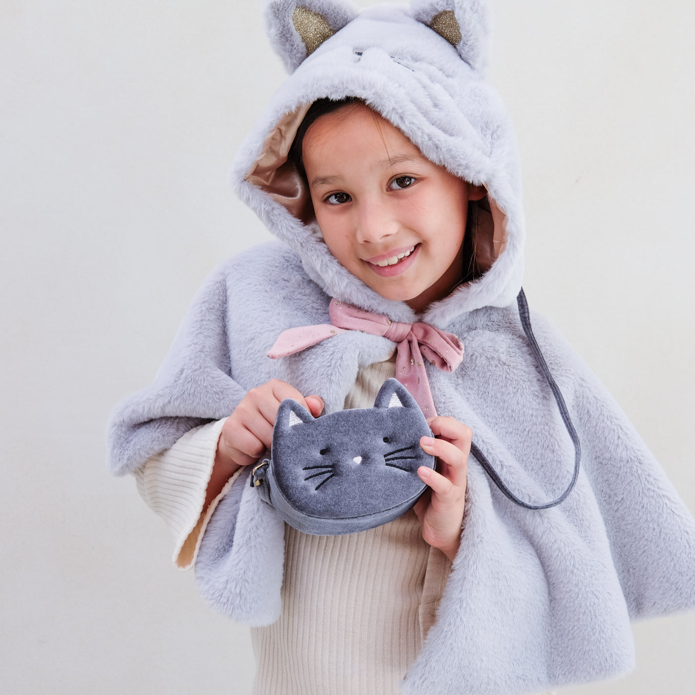 Little girl wearing hooded furry grey cat cape with pink velvet bow and gold glitter ears, complete with furry tail and satin lining, holding soft grey velvet cat handbag