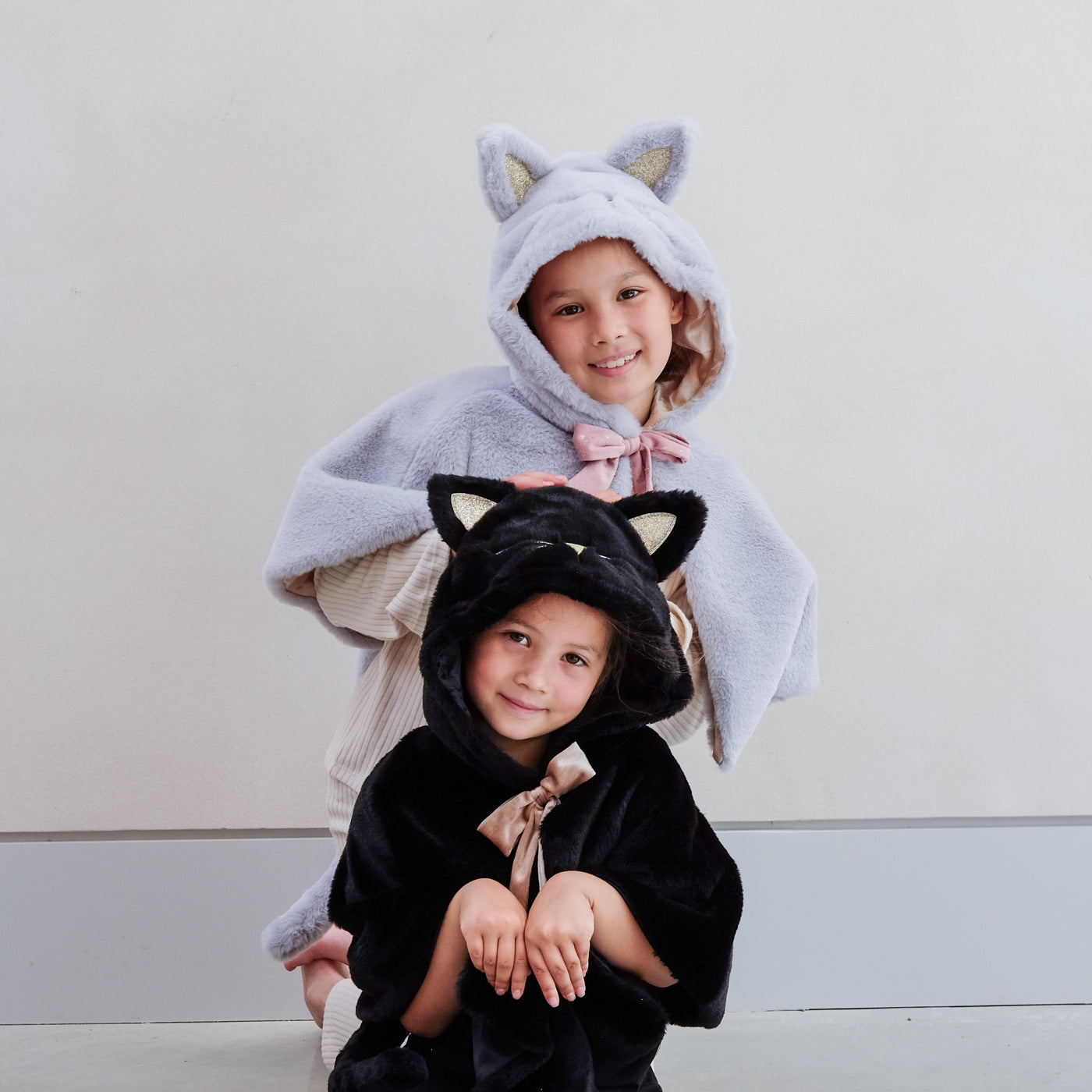 Two little girls in fluffy dressing up cat capes with hoods, one black, one grey