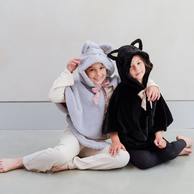 Two little girls wearing fluffy dressing up cat costumes, one grey and one black