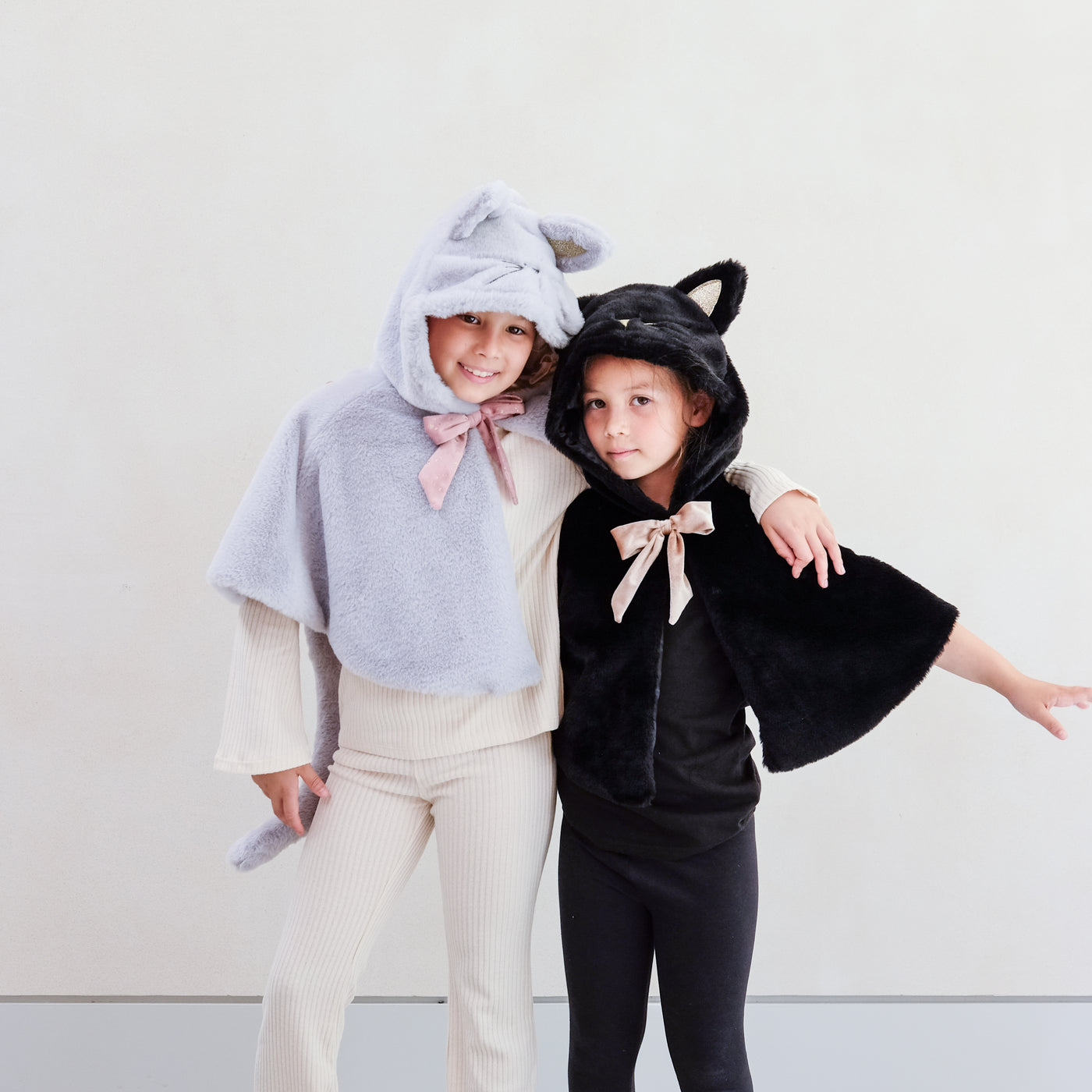 Two little girls wearing fluffy dressing up cat costumes, one grey and one black