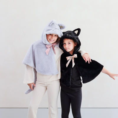Two little girls wearing fluffy dressing up cat costumes, one grey and one black
