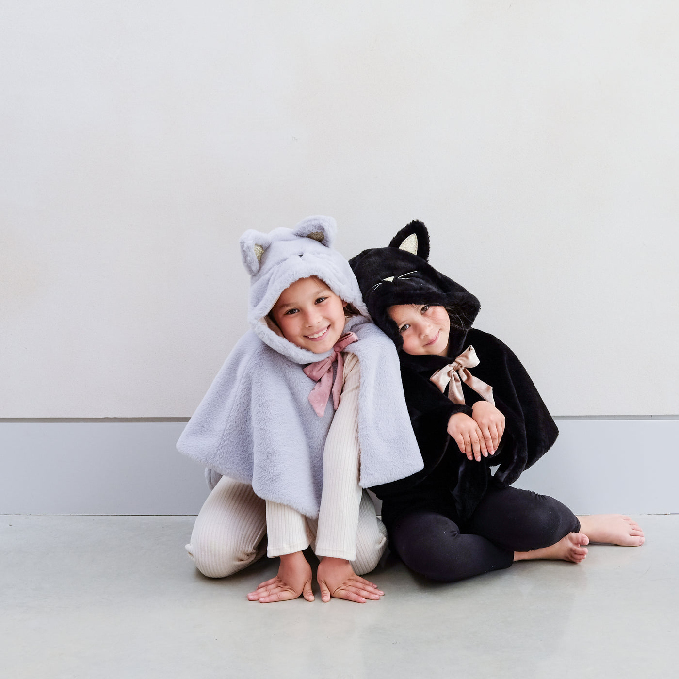 Two children playing wearing black and grey furry cat dressing up capes