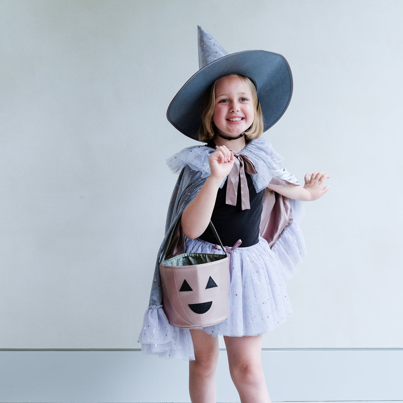little girl holding a pumpkin trick or treat bag for halloween against a plain background